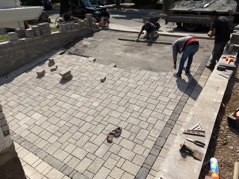 Workers installing paver bricks on a residential driveway or patio during daytime construction