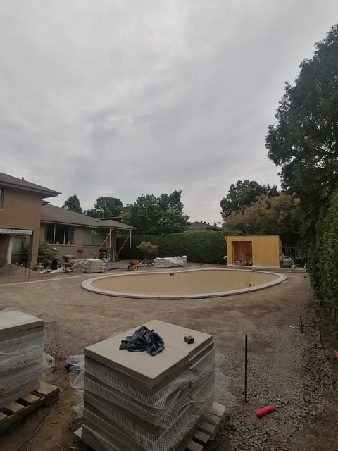 Residential backyard under construction with circular pool structure, building materials, and yellow equipment shed visible