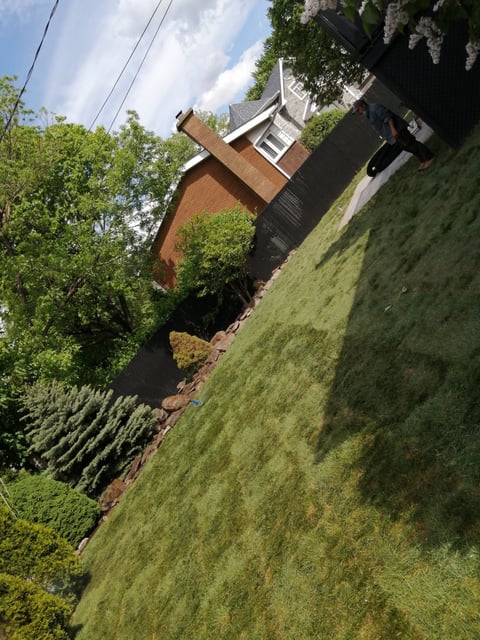 Red brick house with pitched roof nestled among green trees and sloped lawn on a hillside