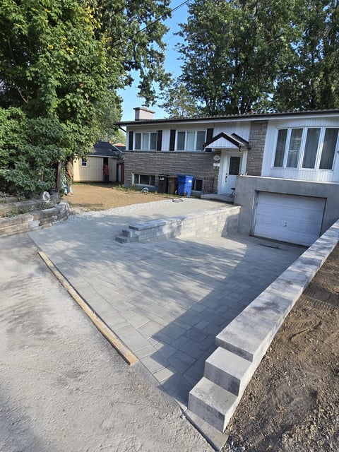 Contemporary brick house with newly paved driveway and garage, surrounded by mature trees on a residential lot