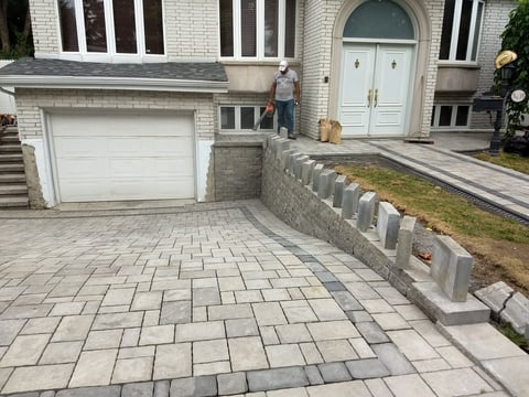 Modern brick home with white garage door, paved driveway, and concrete retaining wall with steps leading to white entrance door